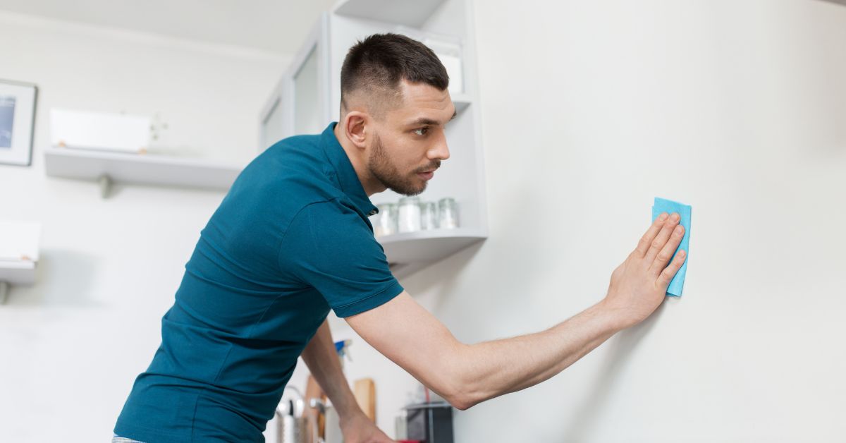 mężczyzna w niebieskiej koszulce czyszczący białą ścianę w jasnej kuchni