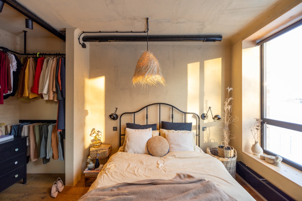 Przytulna sypialnia w stylu boho z naturalnymi dodatkami, drewnianym łóżkiem i wiszącą lampą z trawy morskiej.